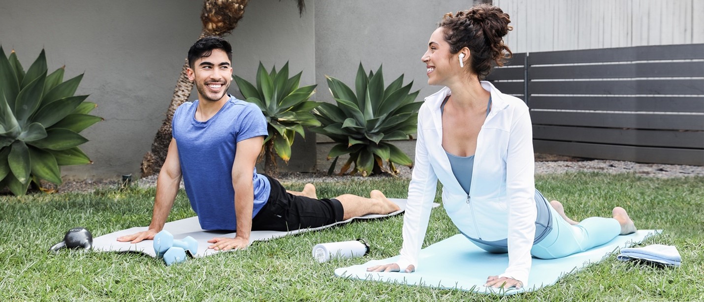 Man and woman doing yoga outdoors smiling at each other.